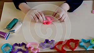 Toddler hands playing colorful play dough with plastic molds of various shapes