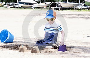 Toddler with Hat & Sunglasses Plays on a Sandy Beach Building Sand Castles