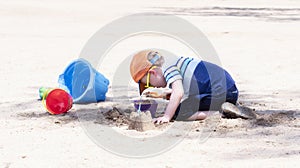 Toddler with Hat & Sunglasses Plays on a Sandy Beach Building Sand Castles