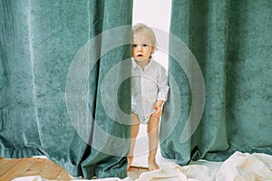 Toddler hides behind a curtain and looks out from it