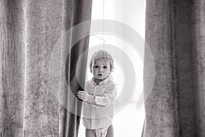 Toddler hides behind a curtain and looks out from it