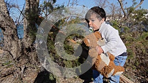 Toddler hugging teddy bear and climbing on the tree thann walk toward camera