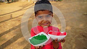 Toddler Indian kid holding two color bowl filled with organic color powder. Beautiful color dye for Holi festival