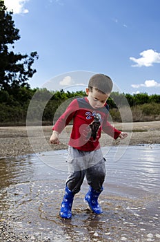 Toddler jumping in a puddle with his new boots