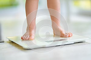 Toddler legs on white scale at home. Bare feet on a weight scale. Measuring and controlling baby weight