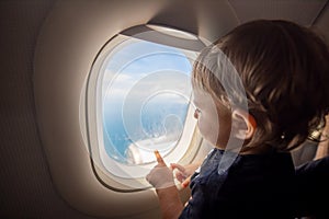 Toddler looks at the ground through the porthole of a flying plane