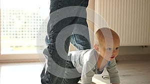 Toddler and mom have fun at home. A baby crawls on the floor and crawls between moms legs