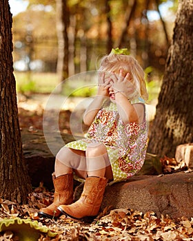 Toddler playing peek-a-boo outside on rock