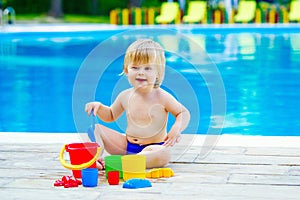 Toddler by the pool palying with toy bucket set