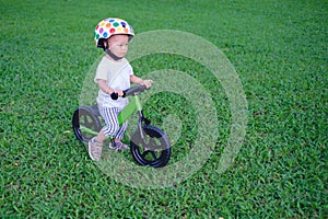 Cute little Asian 1 years / 18 months old baby boy child wearing safety helmet learning to ride his first balance bike at park, ki