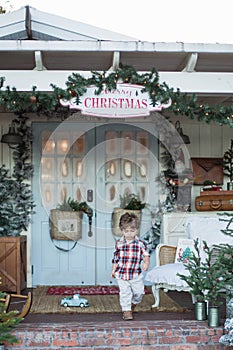 Toddler running out of a white house with a Merry Christmas sign hanging from the roof