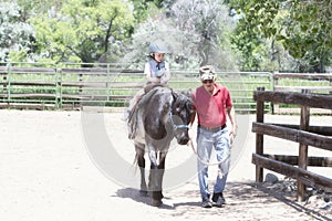 Toddler with a Safety Helmet on Goes on a Pony Ride at a Local Farm with his Horse Being Led Grandfather