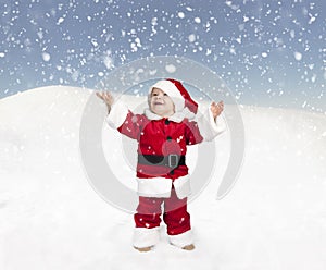 Toddler in santa claus outfit standing in the snow , looking up