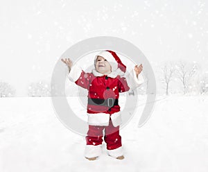 Toddler in santa claus outfit standing in the snow , looking up
