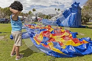 A toddler scratches his head while he stands next to a deflated bounce house