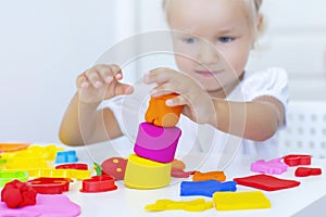 Toddler sculpts from colored plasticine on a white table.