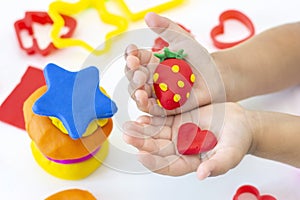 Toddler sculpts from colored plasticine on a white table.