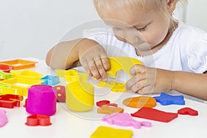 Toddler sculpts from colored plasticine on a white table.