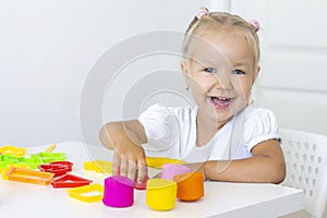 Toddler sculpts from colored plasticine on a white table.