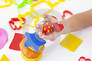 Toddler sculpts from colored plasticine on a white table.