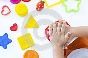 Toddler sculpts from colored plasticine on a white table.