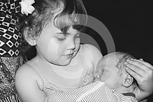 Toddler sister holding her newborn brother black and white