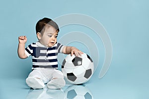 Toddler in striped t-shirt, white pants and booties. He is looking up, sitting on floor against blue background. Close up