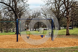 Toddler swings in city park with park bench, person walking and birds and squirrel and a few cars in the background - selective fo