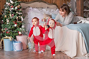 Toddler twins in red reindeer santa claus costumes take their first steps at home with their mother