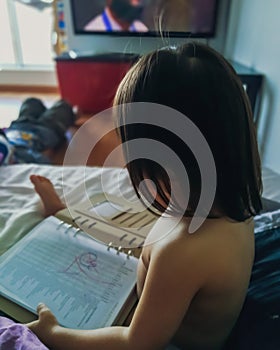 Toddler using book to draw and learn. view from behind