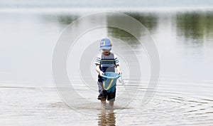 Toddler wearing a Hat & Sunglasses Walks in a Lake Near Shore Hauling Water for Sand Castles