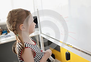 Toddler writing solution of sums on white board at school, educational process