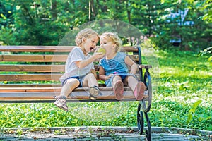 Toddlers boy and girl sitting on a bench by the sea and eat an a