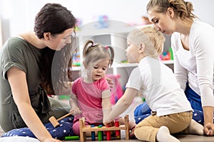 Toddlers and mothers playing with colorful educational toys in nursery room