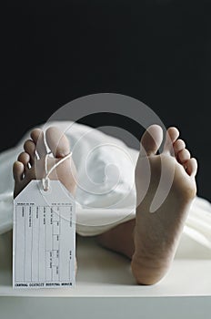 Toe tag hanging on woman lying on table in morgue. Conceptual image shot