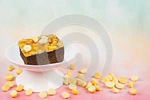 Toffee chocolate cake slice on high plate at left side of frame surrounding nut seeds on colorful background for dessert break