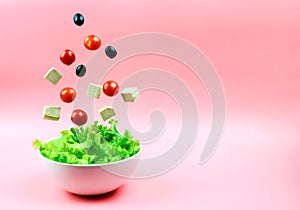 Tofu cheese, cherry tomatoes and olives flying out of the white bowl on a pink background. Concept of a healthy diet.