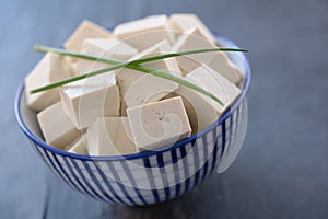 Cubes of tofu in a bowl with green onion leafs