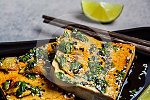 Tofu with marinade of soy sauce, ginger, spices and sesame seeds in black plate