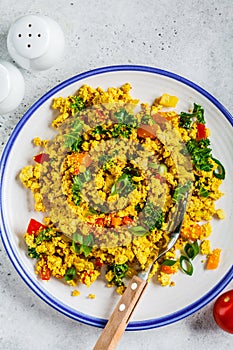 Tofu scramble with vegetables in a white plate, top view. Vegan Alternative fried eggs