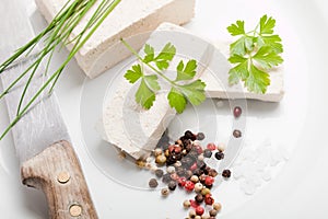 Tofu slices with parsley, salt, pepper and old knife on white background