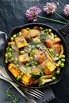 Tofu with vegetables sprinkled with herbs and edible flowers, top view. Vegan dish delicious and nutritious.