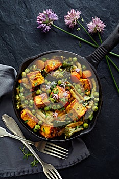 Tofu with vegetables sprinkled with herbs and edible flowers, top view. Vegan dish delicious and nutritious.