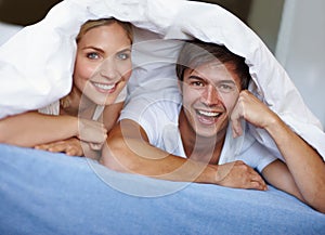 Together is a great place to be. a happy young couple enjoying a playful moment underneath the duvet.