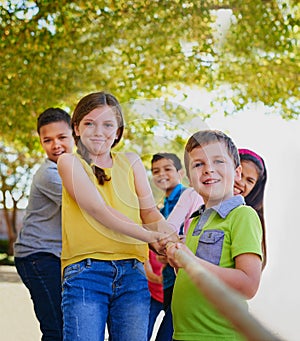 Together we are much stronger. a diverse group of children playing tug of war outside.