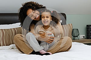 Togetherness Concept. Cheerful african american mother and daughter playing together on bed
