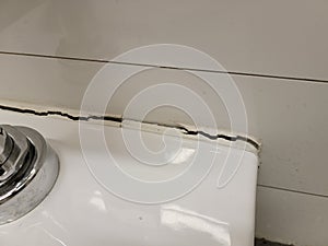 toilet in bathroom with crack in the wall or caulk