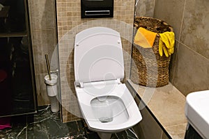 Toilet bowl, basket with rags and gloves and toilet brush in a bathroom