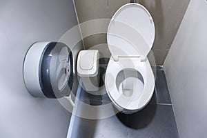 Toilet bowl in a modern bathroom with bins and toilet paper