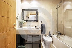 Toilet with light colored marble tiles, veined marble cabinet and black gloss wood base, framed mirror and walk-in shower with